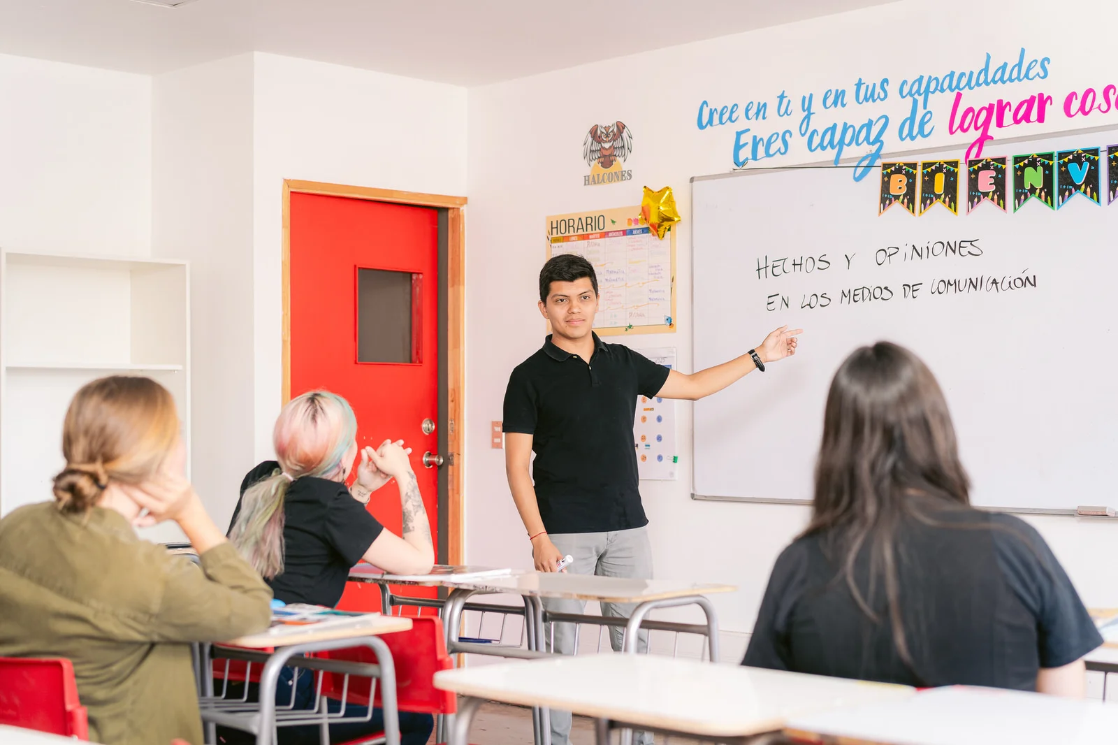 Profesor en pizarra frente a estudiantes, aula con puerta roja — Elige Educar Mineduc