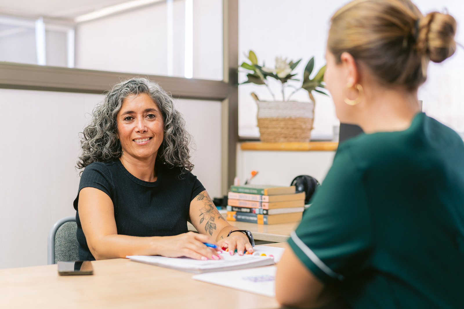 Profesora conversando con colega en escritorio — Elige Educar Mineduc